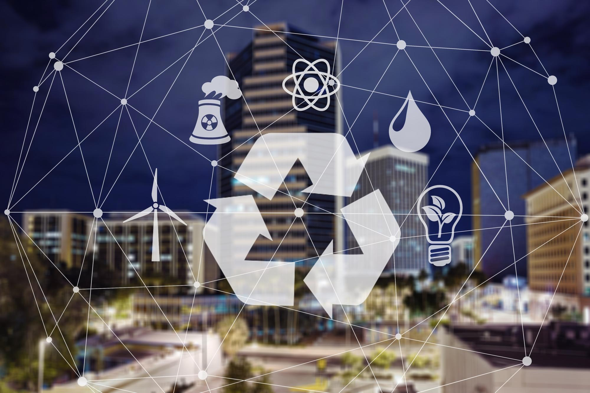 Ikona recyklingu z symbolami energii, atomu, wody, elektrowni jądrowej, turbiny wiatrowej i żarówki na tle nocnego miasta.